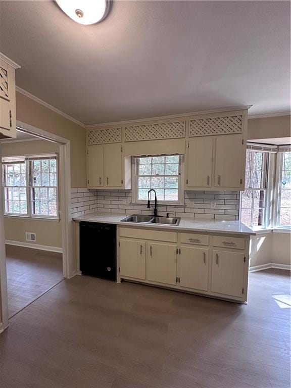 kitchen featuring black dishwasher, ornamental molding, wood finished floors, light countertops, and a sink