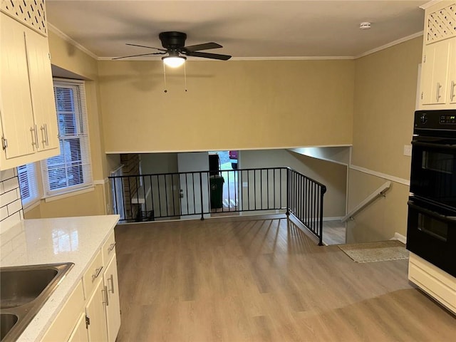 kitchen featuring crown molding, dobule oven black, light wood-style floors, white cabinetry, and a sink