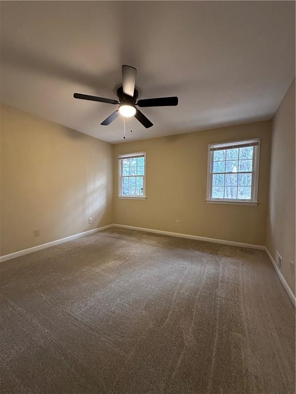 carpeted empty room featuring a ceiling fan, visible vents, and baseboards