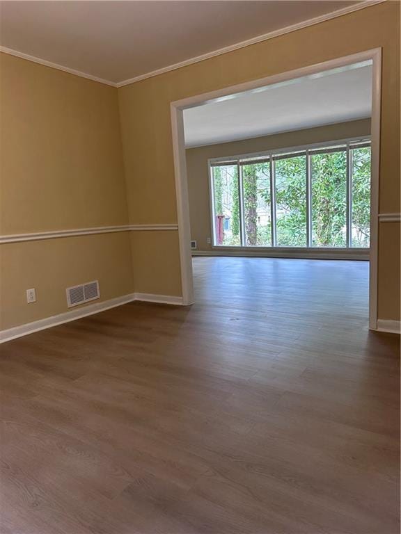 spare room with baseboards, wood finished floors, visible vents, and crown molding