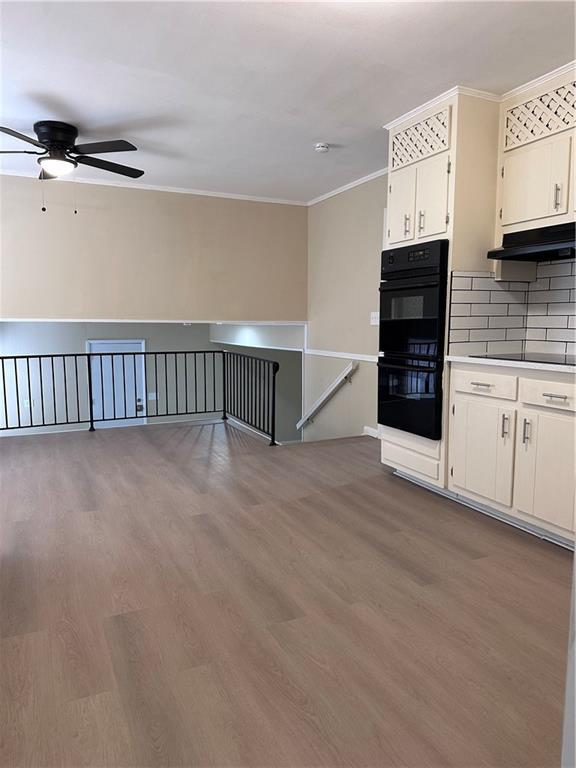 kitchen featuring crown molding, under cabinet range hood, black appliances, and wood finished floors