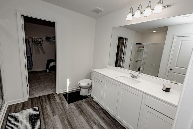 bathroom featuring a stall shower, toilet, wood finished floors, a spacious closet, and vanity