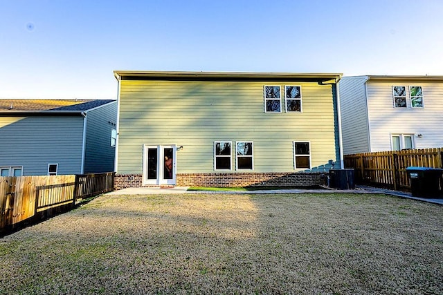 back of property with a fenced backyard, central AC, a lawn, and brick siding