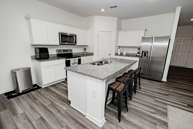 kitchen with visible vents, appliances with stainless steel finishes, light wood-style floors, a sink, and a kitchen breakfast bar