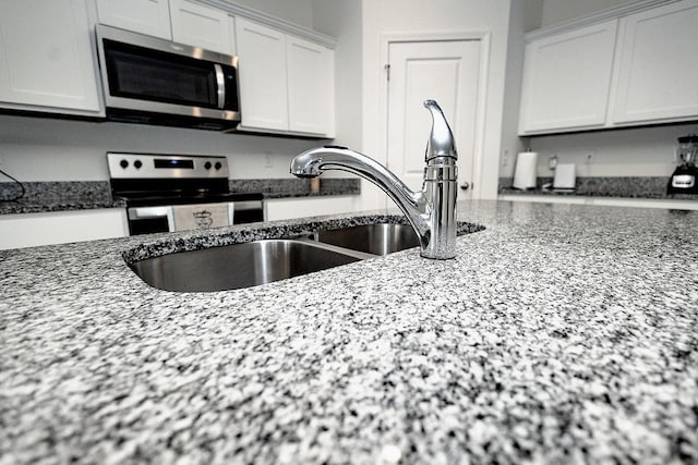 kitchen featuring appliances with stainless steel finishes, white cabinetry, a sink, and dark stone countertops