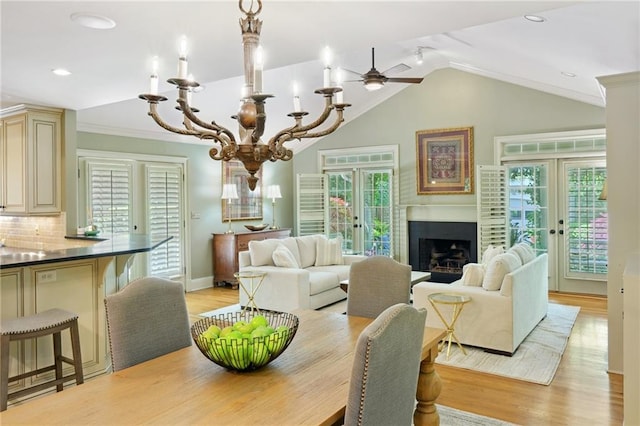 dining room featuring lofted ceiling, light wood-style floors, a fireplace, french doors, and ceiling fan with notable chandelier