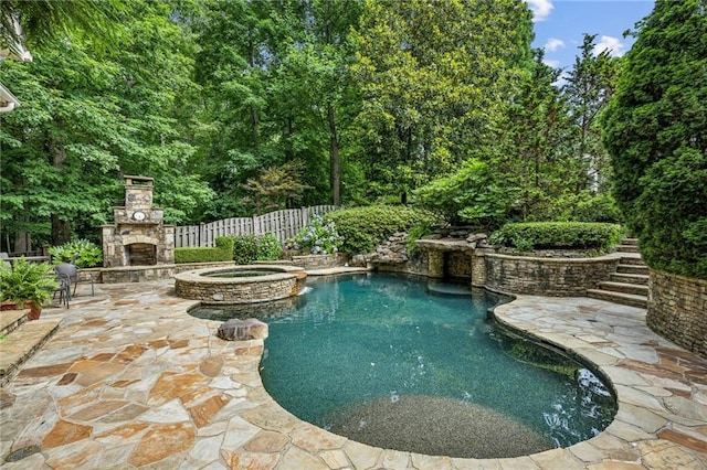 view of swimming pool with fence, an outdoor stone fireplace, a pool with connected hot tub, and a patio area