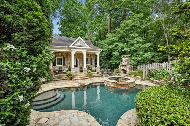 view of swimming pool with fence, an outdoor stone fireplace, a pool with connected hot tub, and a patio area