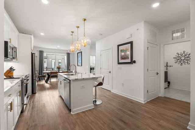 kitchen with sink, appliances with stainless steel finishes, hanging light fixtures, white cabinets, and a center island with sink