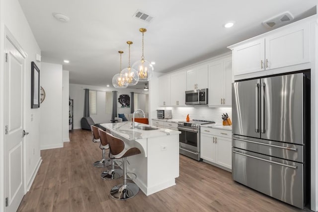 kitchen featuring sink, hanging light fixtures, stainless steel appliances, an island with sink, and white cabinets