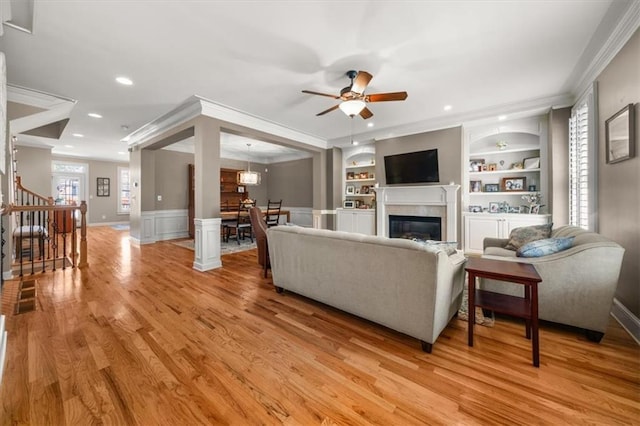 living room featuring stairs, crown molding, built in shelves, and light wood-style floors