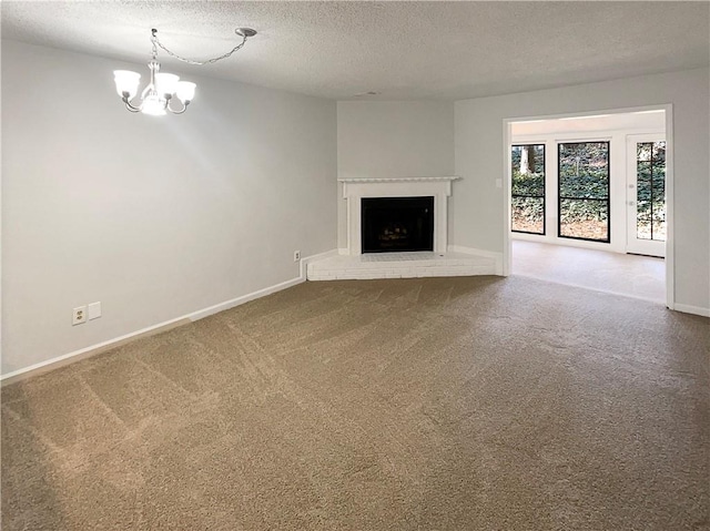 unfurnished living room with an inviting chandelier, a fireplace, a textured ceiling, and carpet