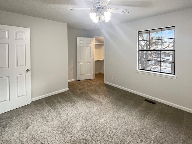 unfurnished bedroom with ceiling fan, dark colored carpet, a textured ceiling, a spacious closet, and a closet