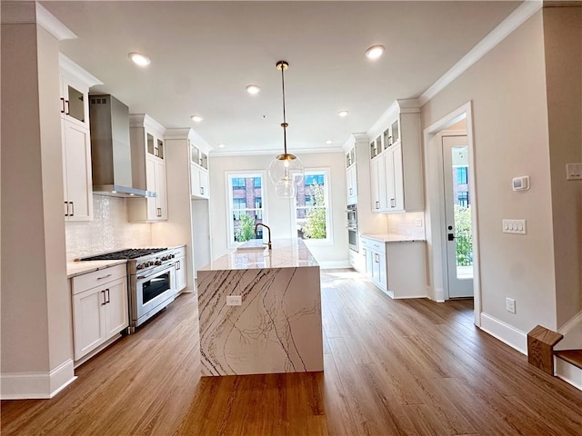 kitchen featuring pendant lighting, an island with sink, wall chimney range hood, light hardwood / wood-style flooring, and high end stainless steel range