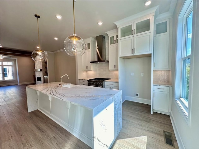 kitchen with sink, an island with sink, high end black range, wall chimney exhaust hood, and decorative light fixtures