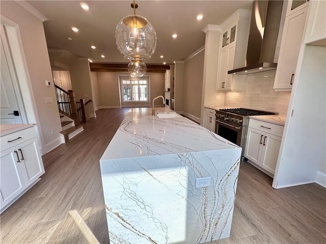 kitchen featuring hanging light fixtures, white cabinetry, wall chimney exhaust hood, a large island, and sink