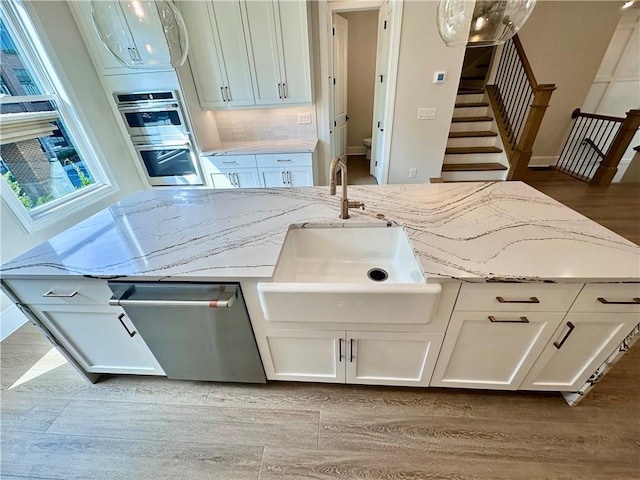 kitchen featuring appliances with stainless steel finishes, white cabinetry, light stone counters, light hardwood / wood-style flooring, and sink