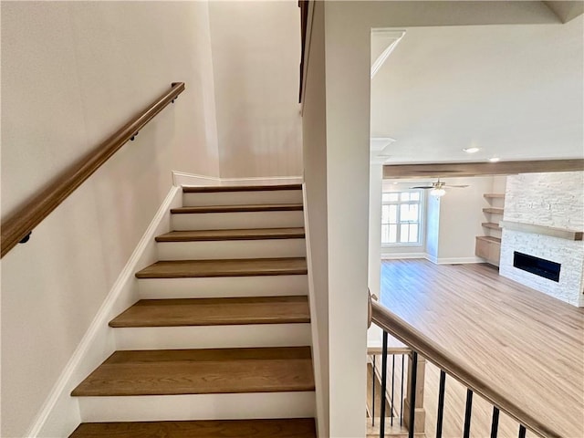 stairway with wood-type flooring, a fireplace, and ceiling fan