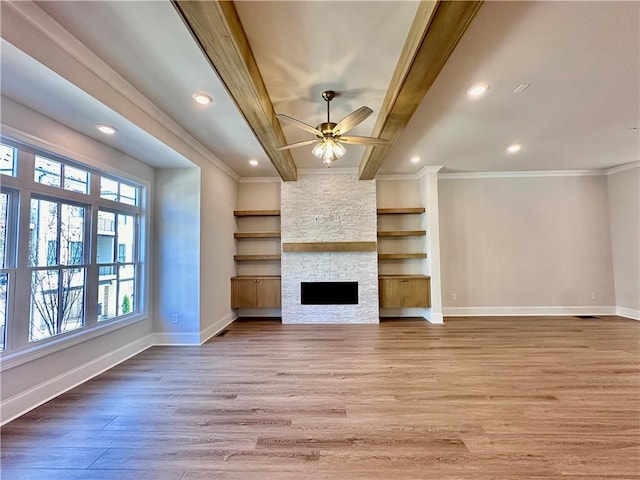 unfurnished living room with ceiling fan, beamed ceiling, a fireplace, light wood-type flooring, and crown molding