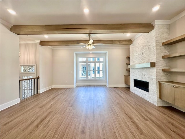 unfurnished living room with ceiling fan, beamed ceiling, light hardwood / wood-style flooring, a fireplace, and crown molding