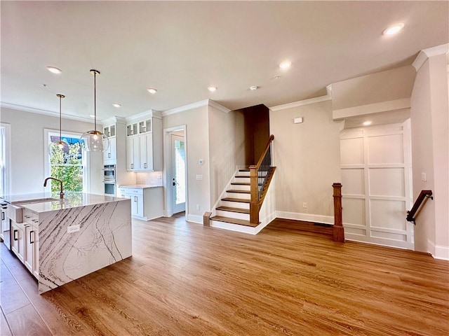 kitchen featuring white cabinetry, an island with sink, pendant lighting, hardwood / wood-style flooring, and ornamental molding