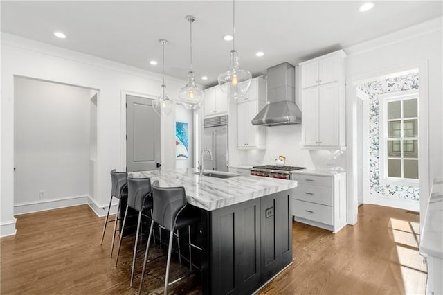 kitchen featuring stainless steel appliances, wall chimney exhaust hood, a sink, a kitchen island with sink, and dark wood-type flooring