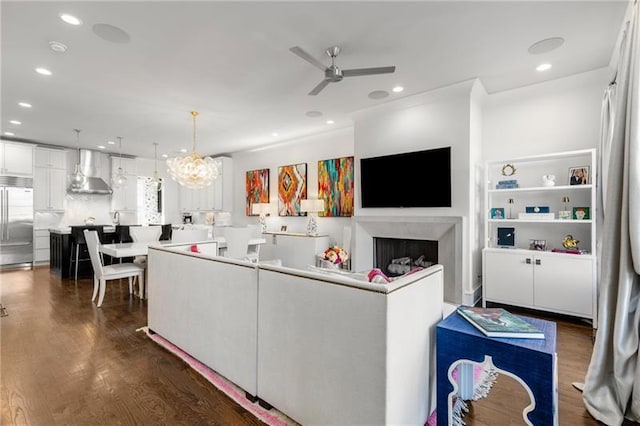 kitchen featuring dark wood-style flooring, stainless steel built in fridge, wall chimney range hood, a fireplace, and white cabinetry