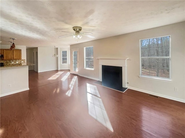 unfurnished living room featuring a textured ceiling, dark hardwood / wood-style flooring, a wealth of natural light, and ceiling fan