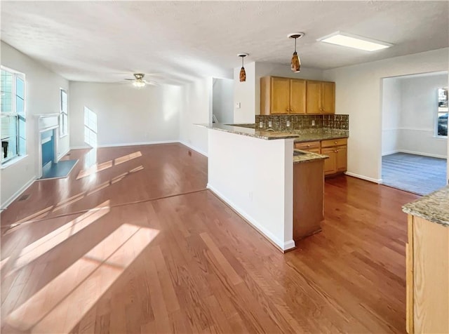 kitchen with kitchen peninsula, decorative backsplash, decorative light fixtures, and hardwood / wood-style flooring