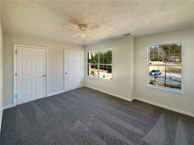 unfurnished bedroom with dark colored carpet, ceiling fan, a textured ceiling, and multiple windows