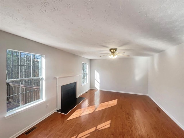 unfurnished living room with a wealth of natural light, a textured ceiling, ceiling fan, and dark wood-type flooring