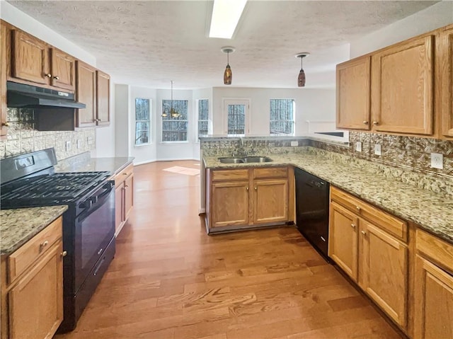 kitchen with sink, hanging light fixtures, kitchen peninsula, black appliances, and hardwood / wood-style flooring