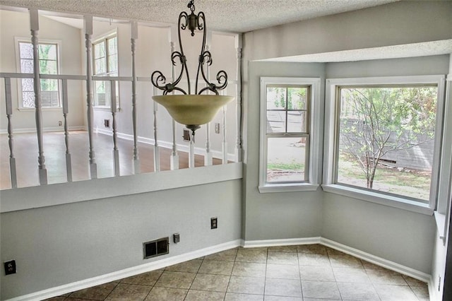 unfurnished dining area with a textured ceiling, visible vents, a chandelier, baseboards, and tile patterned flooring