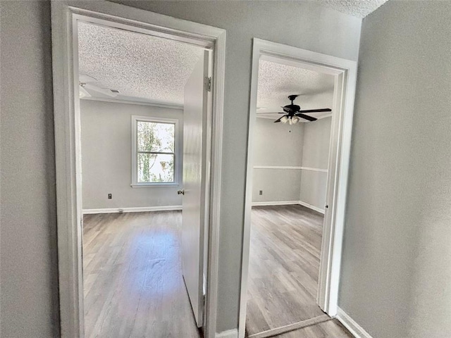 hall with baseboards, wood finished floors, and a textured ceiling