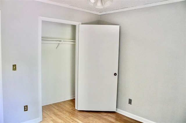 unfurnished bedroom featuring a closet, baseboards, light wood-style flooring, and crown molding