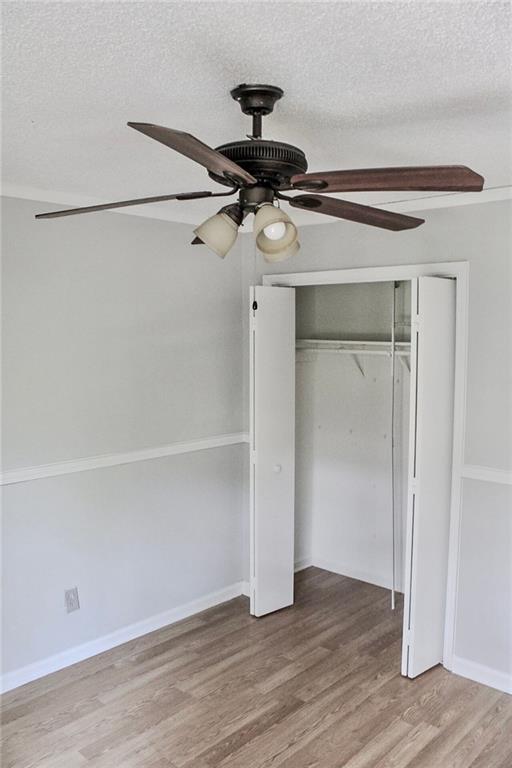 unfurnished bedroom with a closet, a textured ceiling, baseboards, wood finished floors, and a ceiling fan