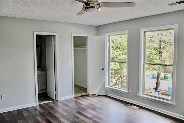 unfurnished bedroom featuring connected bathroom, a textured ceiling, dark wood-style floors, baseboards, and visible vents
