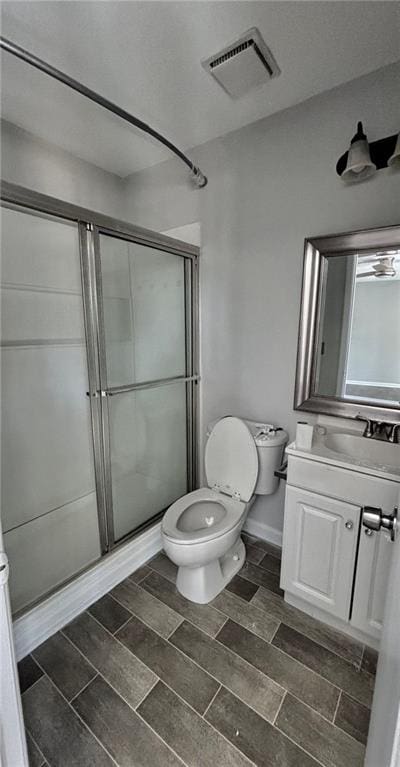bathroom with toilet, vanity, a shower stall, wood tiled floor, and visible vents
