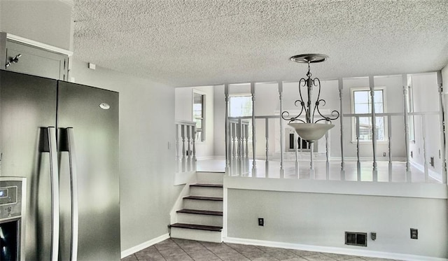 staircase featuring baseboards, a textured ceiling, visible vents, and tile patterned floors