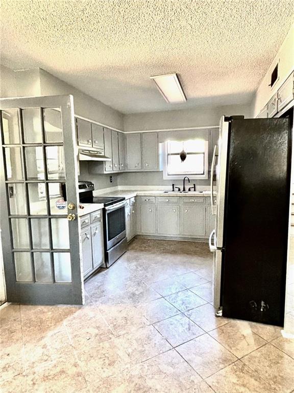 kitchen featuring light countertops, gray cabinets, under cabinet range hood, a sink, and appliances with stainless steel finishes