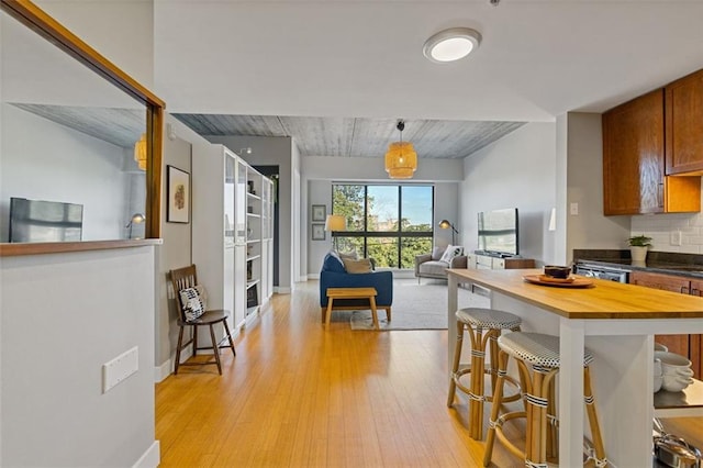 kitchen featuring wooden counters, pendant lighting, light hardwood / wood-style floors, a kitchen bar, and decorative backsplash