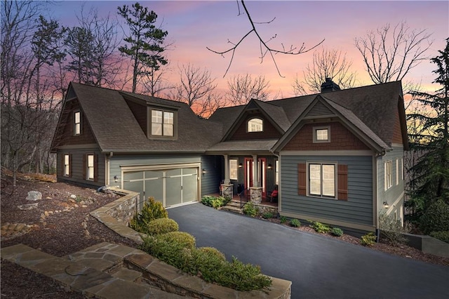 craftsman inspired home with a shingled roof, a chimney, and aphalt driveway