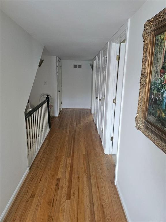 hall with visible vents, baseboards, and wood finished floors