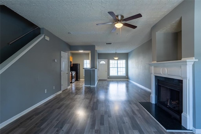 unfurnished living room with dark wood-style flooring, a fireplace with raised hearth, visible vents, a ceiling fan, and baseboards