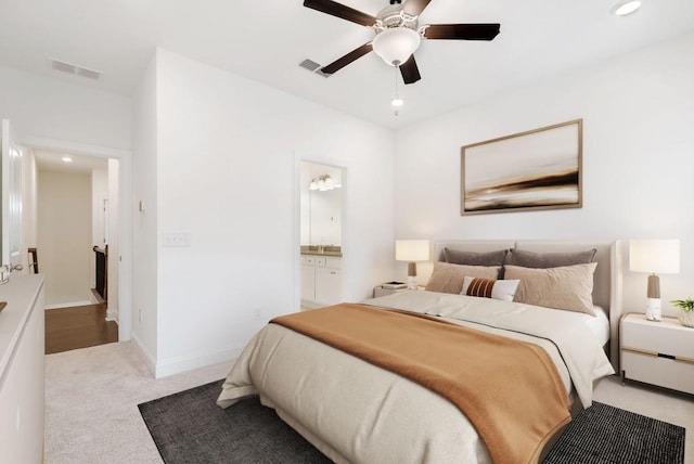 bedroom with ensuite bath, light colored carpet, and ceiling fan