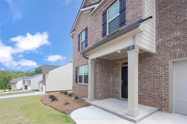 view of exterior entry with a garage, a lawn, and brick siding