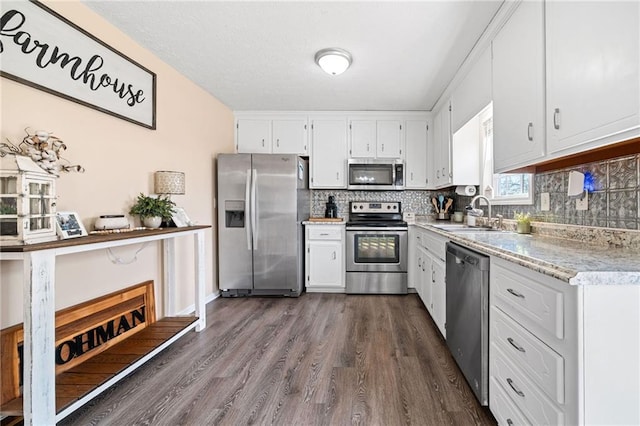 kitchen featuring stainless steel appliances, a sink, white cabinetry, dark wood-style floors, and tasteful backsplash