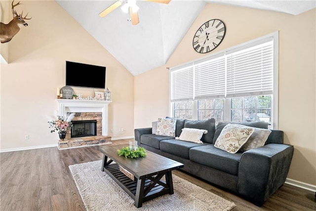 living room featuring high vaulted ceiling, a stone fireplace, wood finished floors, a ceiling fan, and baseboards