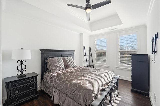 bedroom with a raised ceiling, visible vents, crown molding, and dark wood-style floors