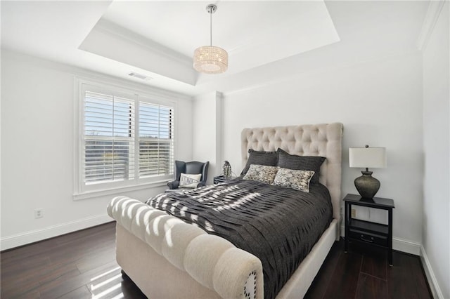 bedroom with a tray ceiling, wood finished floors, visible vents, crown molding, and baseboards